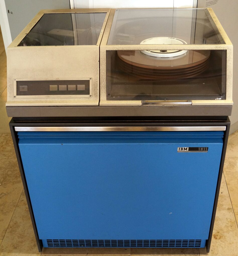 Questa immagine mostra l'IBM 1311 Disk Storage Drive, un dispositivo di memorizzazione dati introdotto nel 1962. Si nota il tipico design di quell'epoca, con la struttura robusta e il pannello frontale che include una finestra trasparente attraverso cui è possibile vedere il disco di memoria interno.